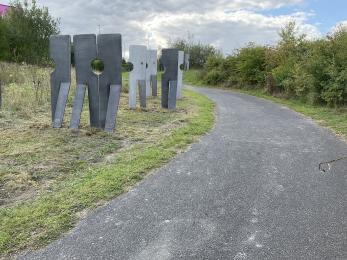 Gently sloping area of the trail after the underpass with steel figures to the left and solid path to the right