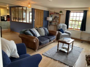 Living room at Albany Cottage showing armchair, sofa and rise and recliner chair with coffee table and rug in the centre .