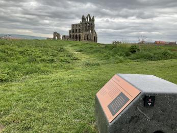 Audio information point on stone plinth with Abbey ruins in the distance.