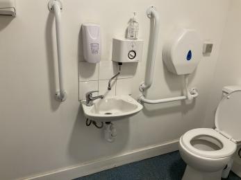 Interior of accessible toilet showing toilet, sink and grab rails.