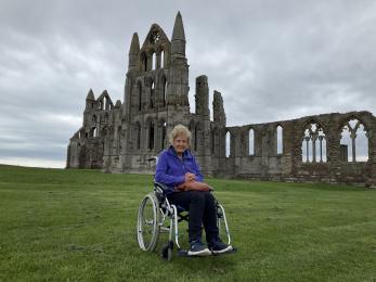 Wheelchair user on grassed area with Abbey ruins in the background.