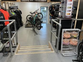 Interior view of lower area in Cycle Hub shop showing steps in the foreground, cycle display and level access entry point.