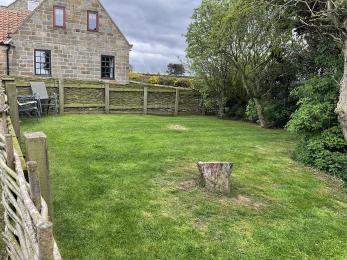 Grassed garden area, containing a tree stump and set of table and chairs, surrounded by fencing.