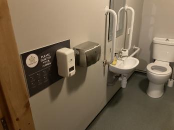 Accessible toilet showing toilet, grab rails, sink and automatic hand dryer.