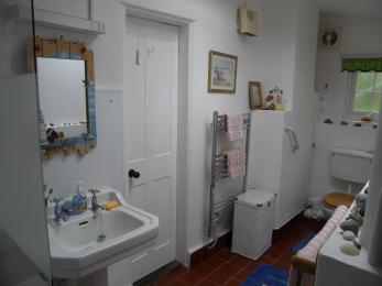 The bathroom is long and narrow with a cardinal tile floor. There is a handrail to the right of the toilet . 