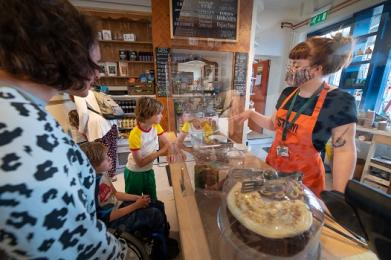 Customers at the cake display counter, talking to staff in an orange apron