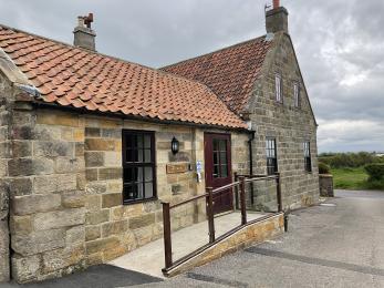 External view of Albany Cottage showing stone exterior and gently sloping access ramp up to main entrance.