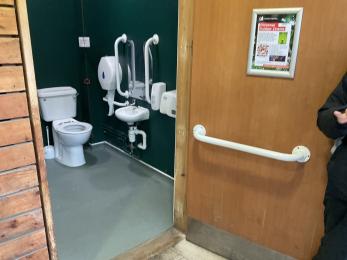 Accessible toilet showing outward opening door with contrasting white grab rail and toilet interior beyond.