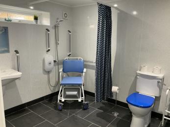 En-suite wet room showing toilet with contrasting coloured seat and shower area with  wheeled shower chair.