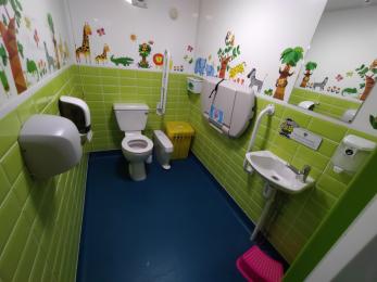 Disabled toilet with baby changing table, bright lighting and adjusted toilet and sink.