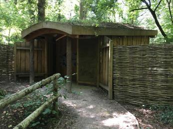 Heronry Hide. A wooden structure with a natural roof. There is a wattle and daub heron mural at the entrance. 