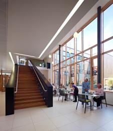 Image of some of the cafe space, tables at large windows and a staircase leading to the offices