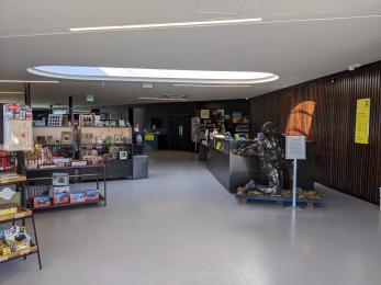 Just inside the main entrance to the museum. There is a desk on the right hand side and shop furniture and shelving to the left.