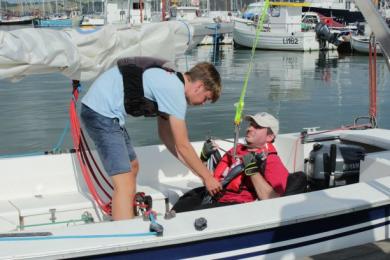 Person now hoisted into beanbag seat in sailing boat alongside a pontoon at Mylor Sailing and powerboat School Falmouth Cornwall
