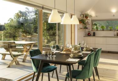 Dining area with table for 8 guests with view outside through full-length windows to terrace and to kitchen