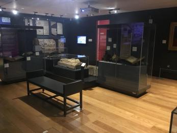Image shows Albany Gallery exhibition from the back. Various glass cases with objects can been seen in the centre of the space