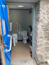 Visitor accessible toilet from outside showing door, toilet and transfer space to left of toilet