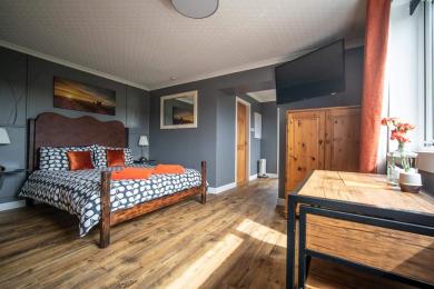 Image of The Grey Suite - kingsize bed, floor area near dining table, wardrobe and tv with bathroom door and bunk room door beyo