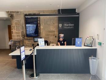 Image shows reception desk and shop till with a member of staff working 