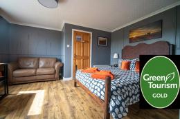Photo of The Grey Suite showing kingsize bed, sofa and wall carvings with a Green Tourism Gold Award logo