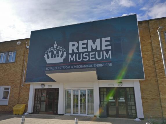 The front entrance of the REME Museum, three sets of double doors above which is a large blue sign with museum logo.