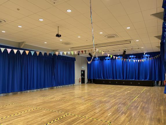 internal image of The Queens Hall with wooden floors and bright blue curtains and multi coloured bunting